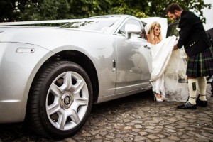 The groom helps his bride out of their Rolls Royce wedding car