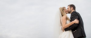 the bride and groom passionately kiss with sky as background