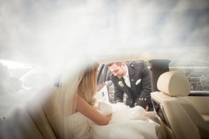 the groom gently helps his bride into their wedding car