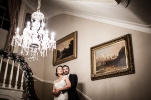 Bride and groom hold each other tightly on staircase illuminated by chandelier