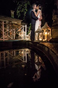 bride and grooms reflection is visible in the water as they kiss near candles