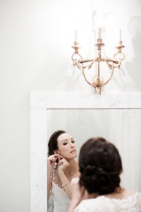 bride puts on her earing in the white marble bathroom