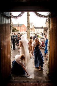 bridesmaids rush to aid the bride whose dress was caught on the ground while leaving the church in warm evening light