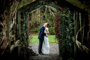 groom kissing the neck of his bride and making her laugh under tunnel of foliage