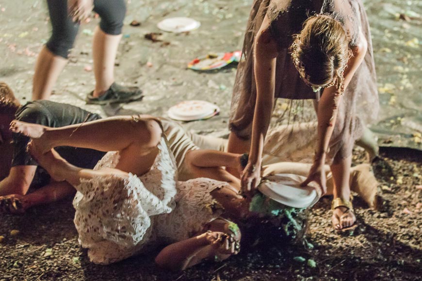 bride lays on the ground as bridesmaid smashes a plate of cake in her face