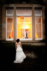 bride outside with groom inside looking out of window