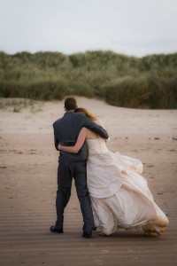 bride and groom blown by wind on beach