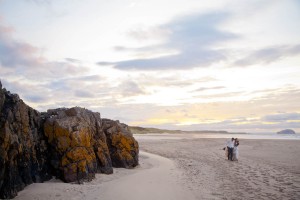 bride and groom walk along beach at sunset