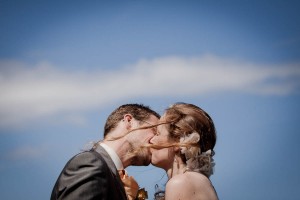 bride and groom kiss at beach wedding on windy day