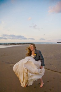 bride in groom's jacket almost blow away on beach at wedding on windy day