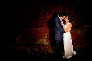 bride and groom kiss outside amidst leaves in dark