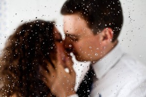 bride and groom kiss behind raindrops on window